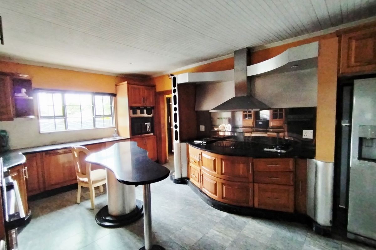 Spacious kitchen featuring wooden cabinetry, granite countertops, a built-in oven, extractor fan, and a central breakfast bar area.
