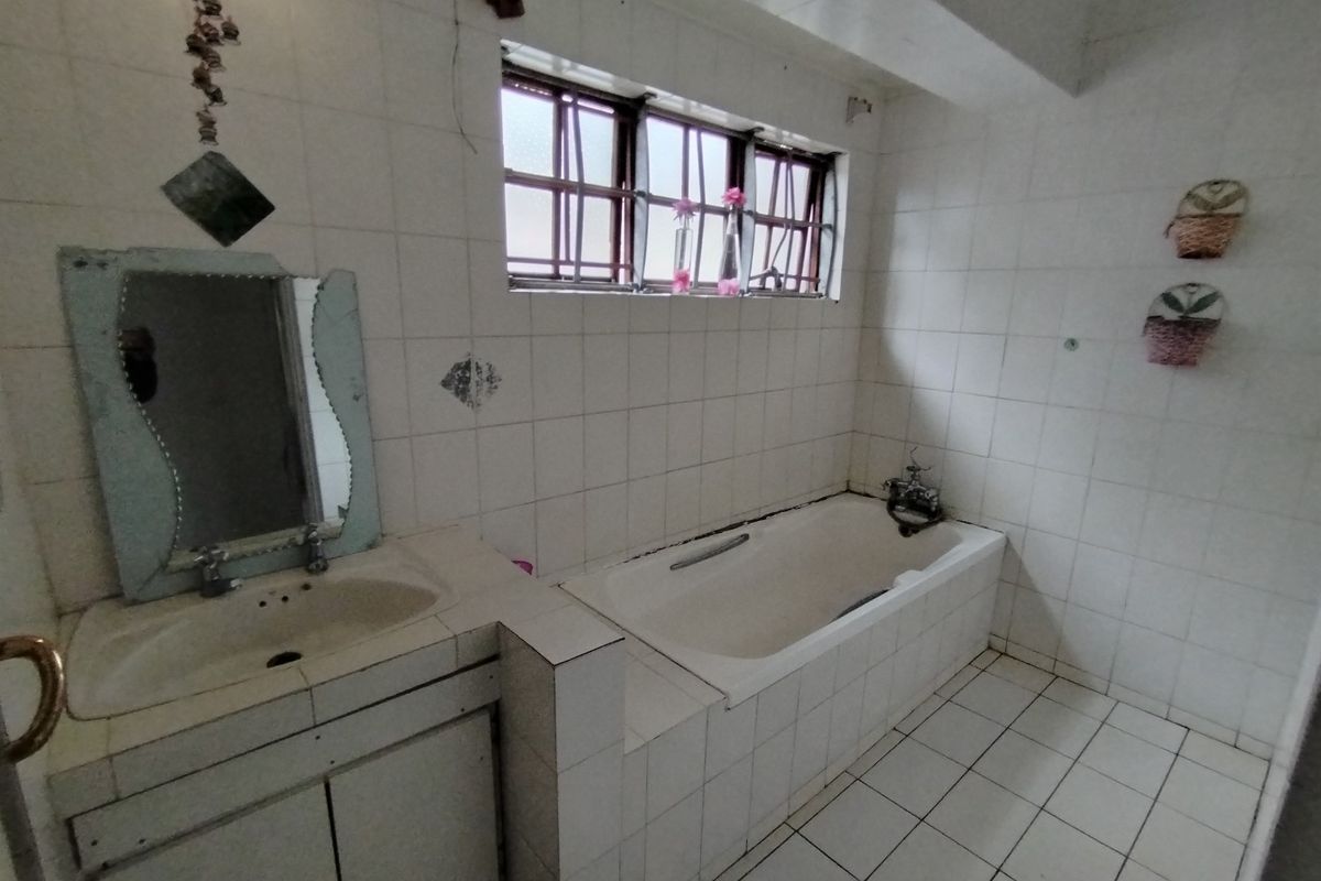 A dated bathroom featuring a built-in vanity, tiled bathtub, and tiled finishes throughout, requiring modernization to improve its aesthetic and functionality.