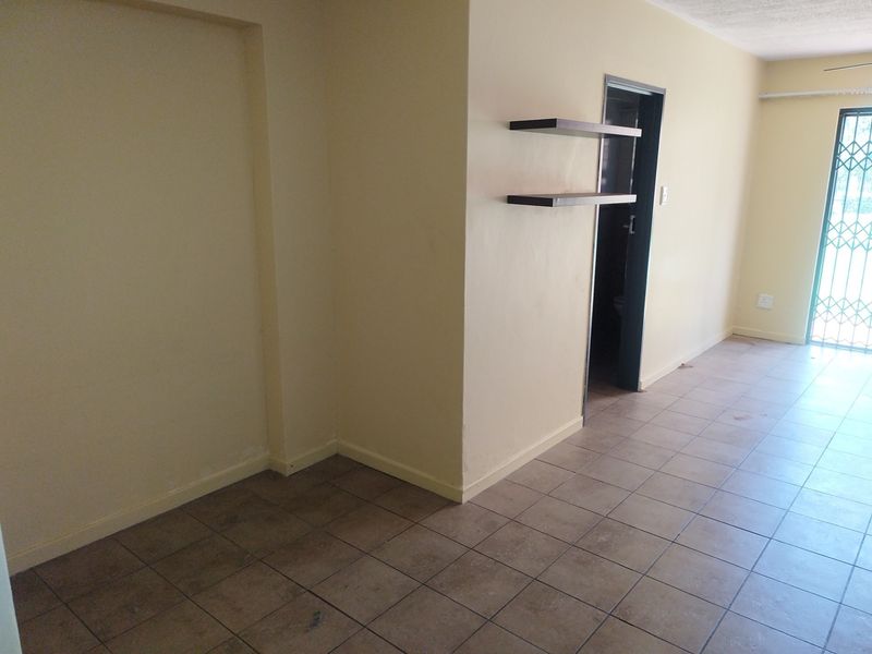 An empty living area featuring ceramic floor tiles, built-in wall shelving, and a security gate leading to the exterior.