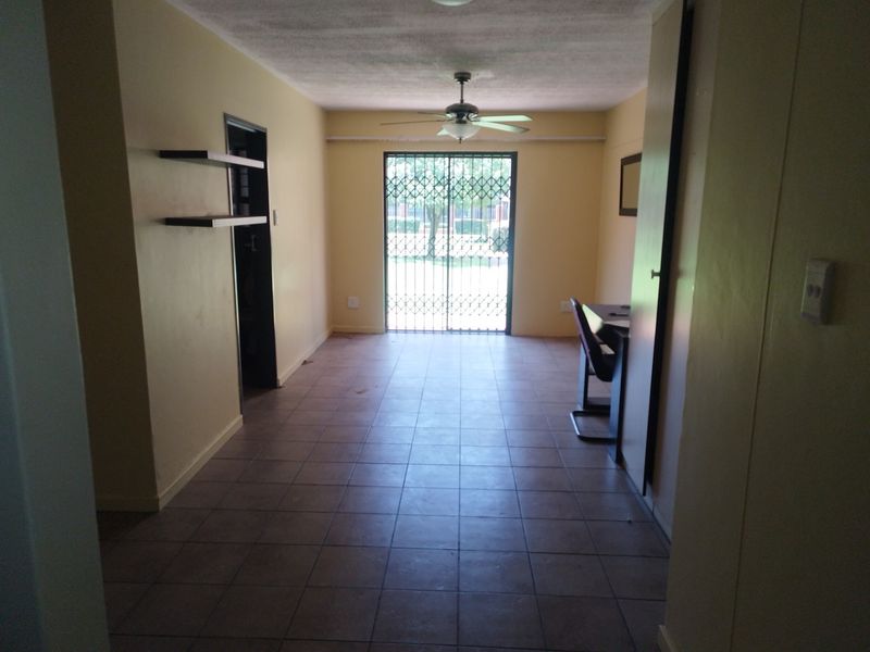 A sparsely furnished living area featuring tiled flooring, a ceiling fan, and a sliding glass door with a security gate leading outdoors.