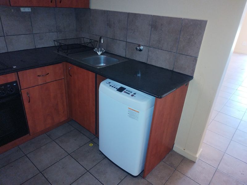A functional laundry area featuring built-in cabinetry, granite countertops, a stainless steel sink, and tiled finishes.
