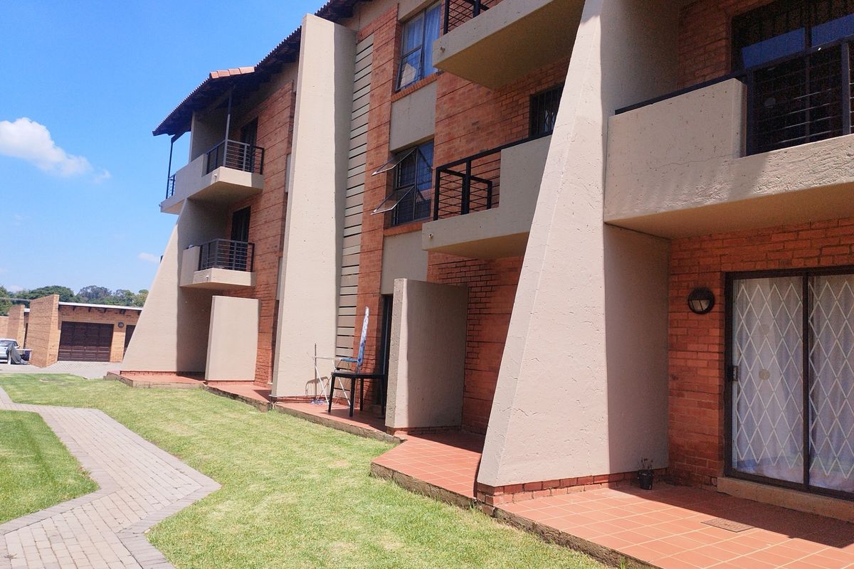 Rear view of a multi-story townhouse complex featuring brick facades, private balconies, ground-floor patios, and a well-maintained lawn with paved walkways.