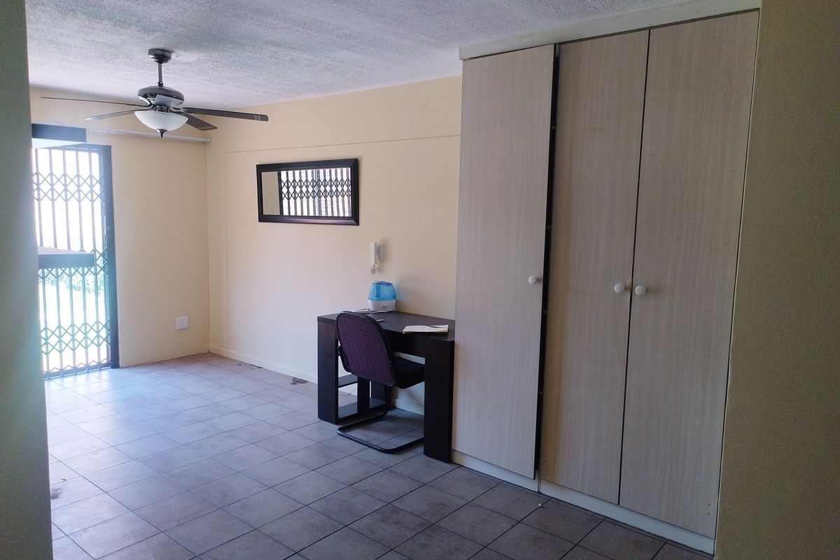 A bedroom featuring built-in cupboards, tiled flooring, a ceiling fan, and a security gate leading to the exterior.