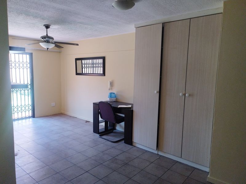 A bedroom featuring built-in cupboards, tiled flooring, a ceiling fan, and a security gate leading to the exterior.