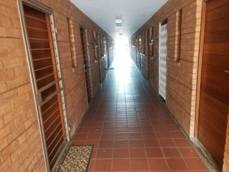 A long, covered exterior-style hallway featuring exposed brick walls, tiled flooring, and multiple security gates leading to individual units.