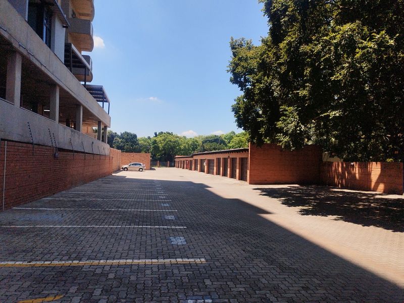 An outdoor parking area featuring a row of individual garage units, paved driveway, and brick boundary walls with electric fencing.