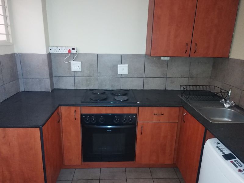 A functional kitchen featuring wood-tone cabinetry, dark laminate countertops, a built-in electric oven and hob, and a stainless steel sink with tiled backsplash.