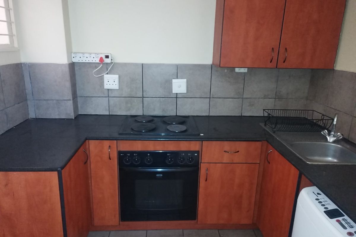 A functional kitchen featuring wood-tone cabinetry, dark laminate countertops, a built-in electric oven and hob, and a stainless steel sink with tiled backsplash.