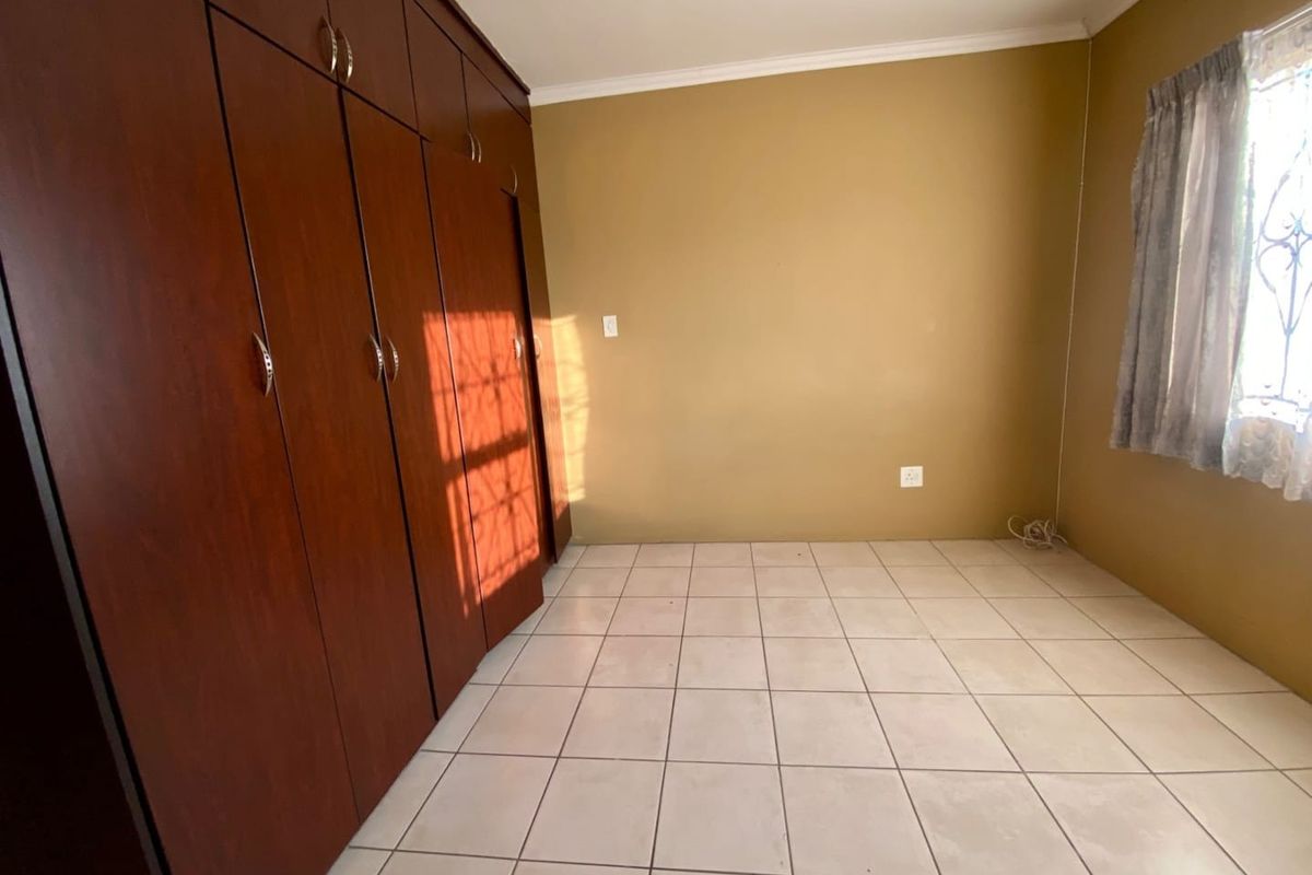 A bright, empty bedroom featuring tiled flooring and extensive built-in wooden cupboards, offering ample storage space.