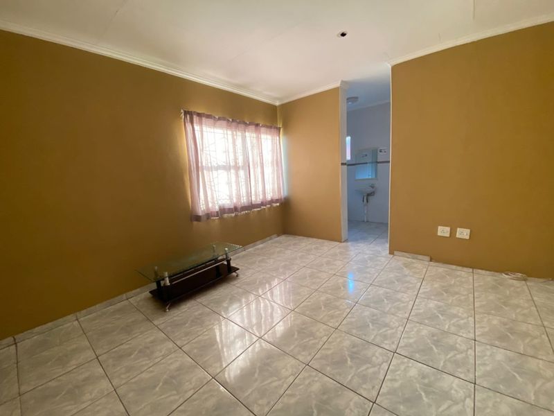 A simple, tiled living area with neutral walls and a view into an adjacent bathroom space.