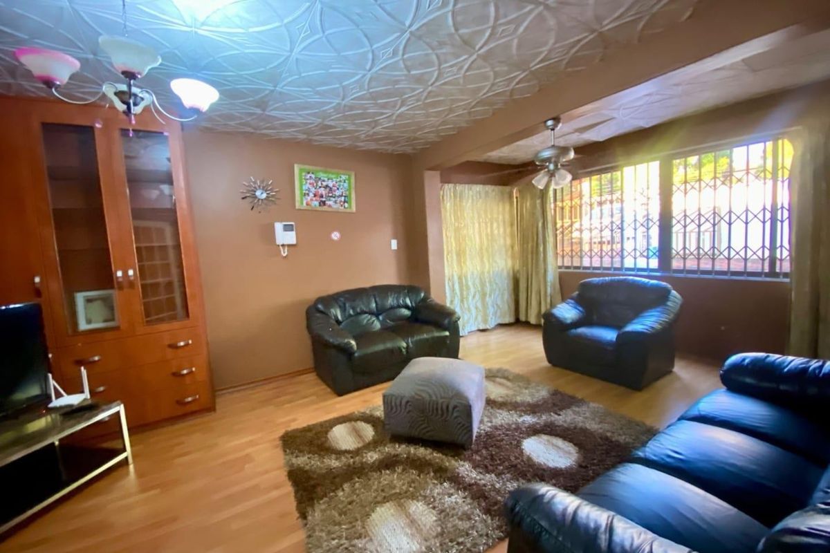 A living room featuring laminate flooring, decorative ceiling tiles, and security bars on the windows, with a built-in display cabinet.