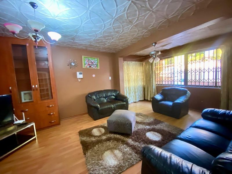A living room featuring laminate flooring, decorative ceiling tiles, and security bars on the windows, with a built-in display cabinet.