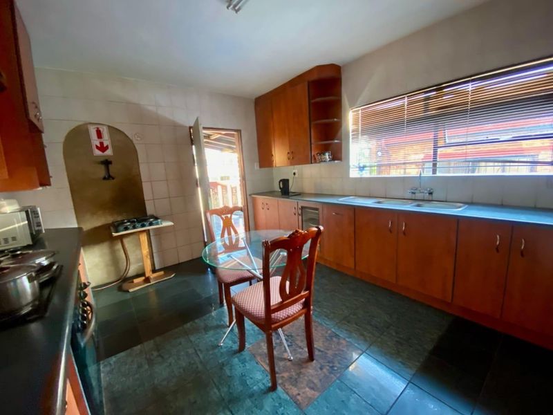 A functional kitchen featuring wooden cabinetry, a double basin sink, and tiled flooring, offering a practical layout with direct access to the exterior.
