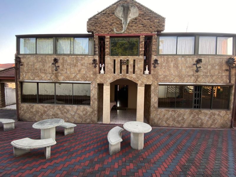 Rear exterior view of a two-story house featuring a unique stone elephant relief, tiled facade, and a paved patio area.