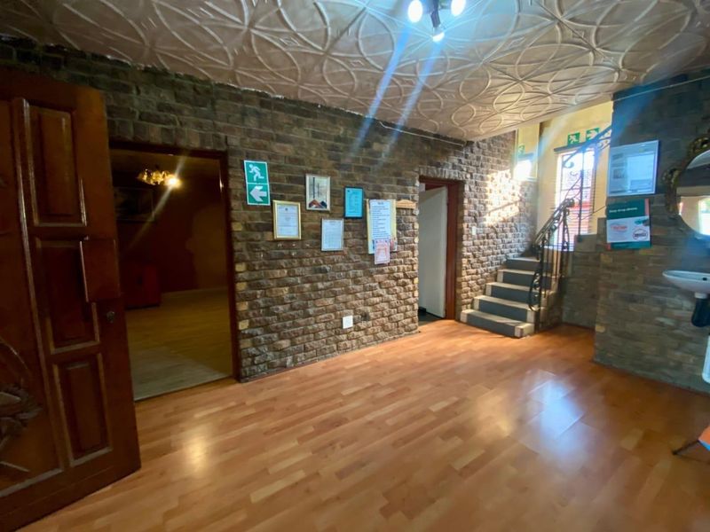Spacious entrance hall featuring exposed brick walls, decorative pressed metal ceiling, laminate flooring, and a staircase with wrought iron railing.