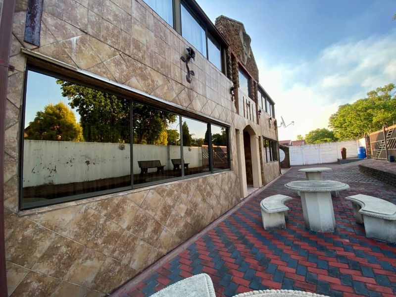 Rear exterior view of the property featuring a tiled facade, large windows, and a paved patio area with boundary walling.