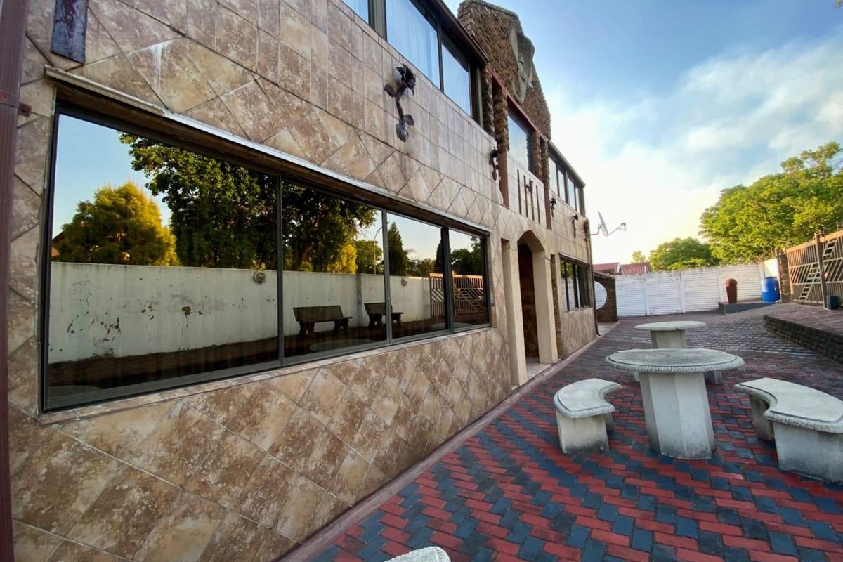 Rear exterior view of the property featuring a tiled facade, large windows, and a paved patio area with boundary walling.