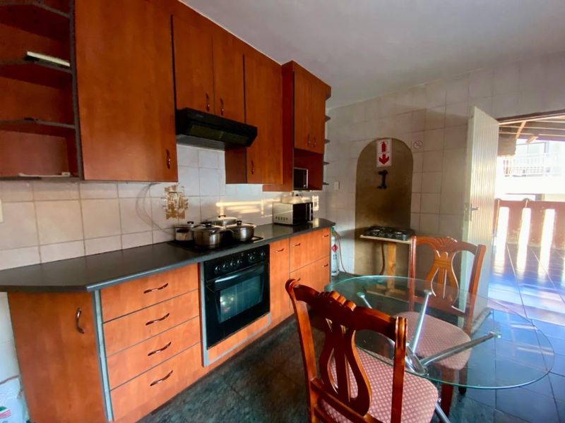 A functional kitchen featuring wood-tone cabinetry, built-in oven with extractor fan, tiled backsplash, and dark floor tiles, offering a practical layout for daily use.