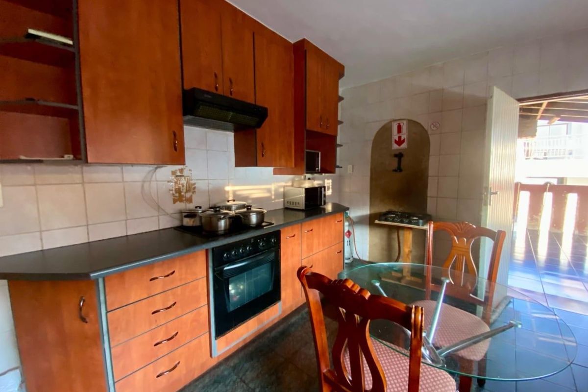 A functional kitchen featuring wood-tone cabinetry, built-in oven with extractor fan, tiled backsplash, and dark floor tiles, offering a practical layout for daily use.