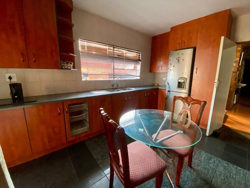 A functional kitchen featuring wood-tone cabinetry, tiled backsplash, and dark floor tiles, offering a practical layout with ample storage space.