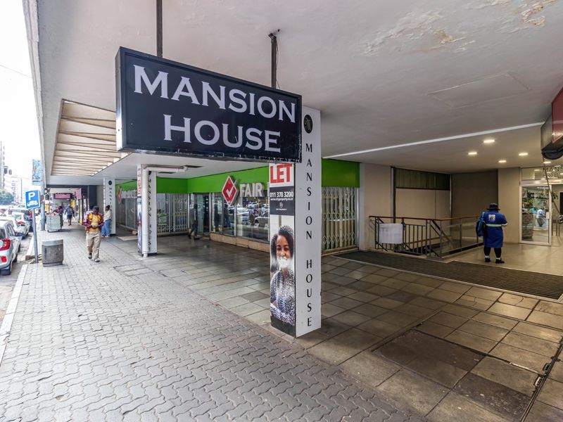 Street-level view of the Mansion House commercial building entrance, featuring paved walkways, prominent signage, and access to the building interior.