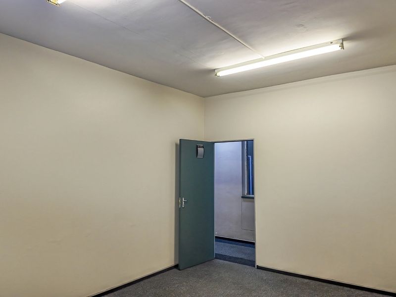 A vacant, neutral-toned office space featuring carpeted flooring and overhead fluorescent lighting, providing a clean and functional commercial work environment.