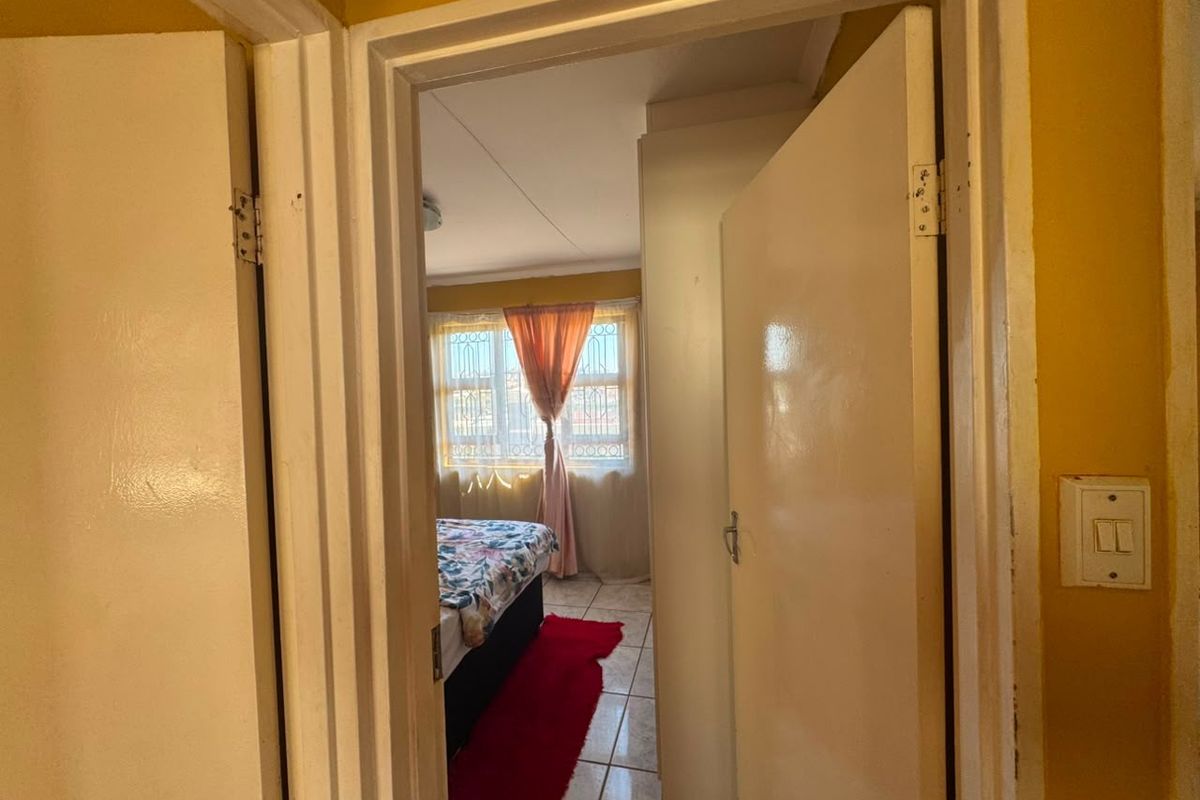 A view through a doorway into a bedroom featuring tiled flooring and security bars on the window.