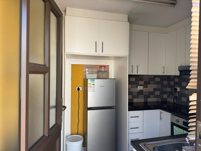 Compact kitchen featuring white cabinetry, dark granite countertops, a tiled backsplash, and built-in oven, offering a functional layout with modern finishes.
