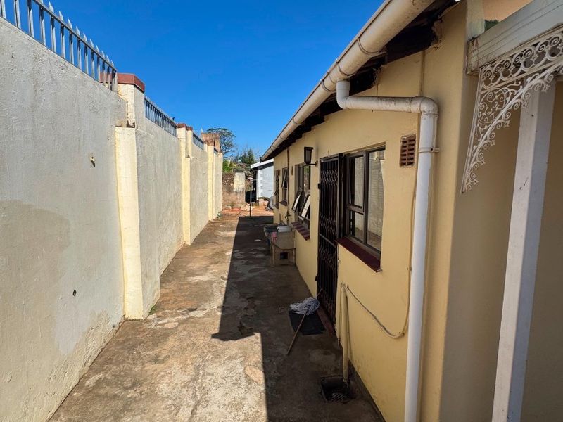 A narrow side passage of the property featuring a concrete boundary wall with security spikes and paved flooring along the exterior building wall.