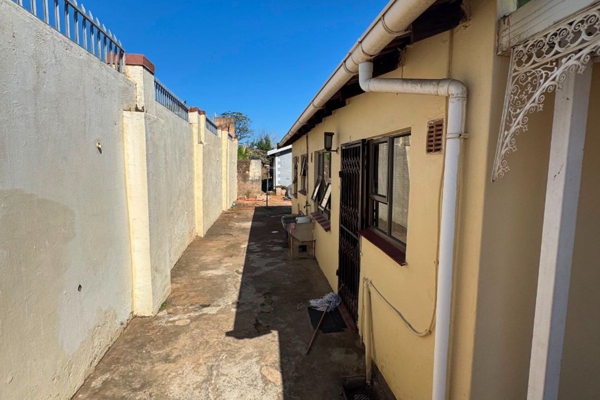 A narrow side passage of the property featuring a concrete boundary wall with security spikes and paved flooring along the exterior building wall.