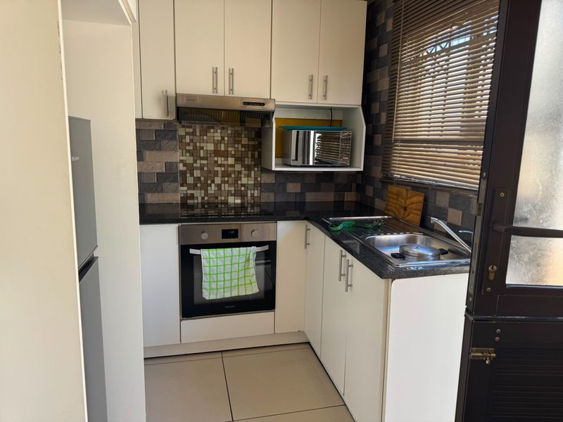 Compact kitchen featuring white cabinetry, granite countertops, built-in oven, extractor fan, and a tiled backsplash with a window providing natural light.