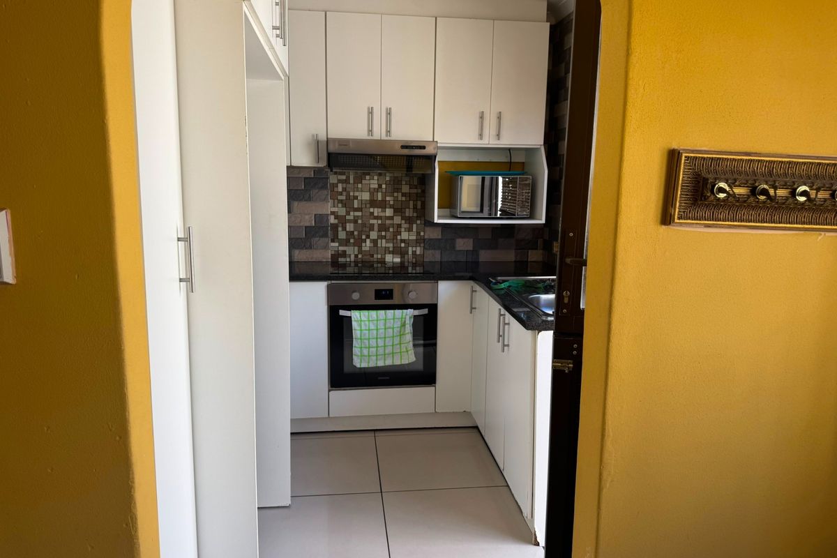 Compact kitchen featuring white cabinetry, granite countertops, mosaic tile backsplash, and integrated stainless steel appliances.