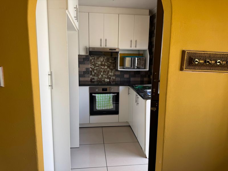 Compact kitchen featuring white cabinetry, granite countertops, mosaic tile backsplash, and integrated stainless steel appliances.