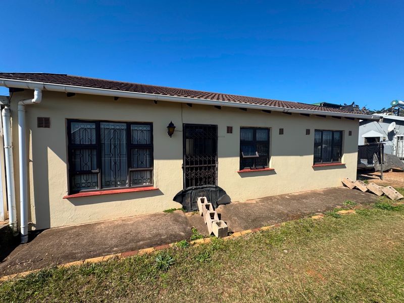 Rear exterior view of the house featuring a tiled roof, security gates on doors and windows, and a concrete pathway along the building perimeter.