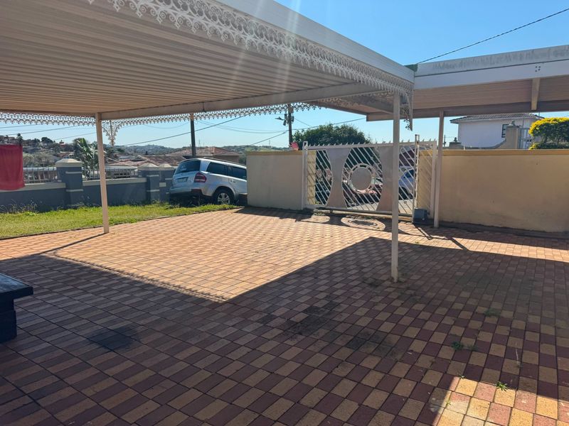 A paved outdoor carport area featuring a covered structure, perimeter walling, and a metal gate entrance.