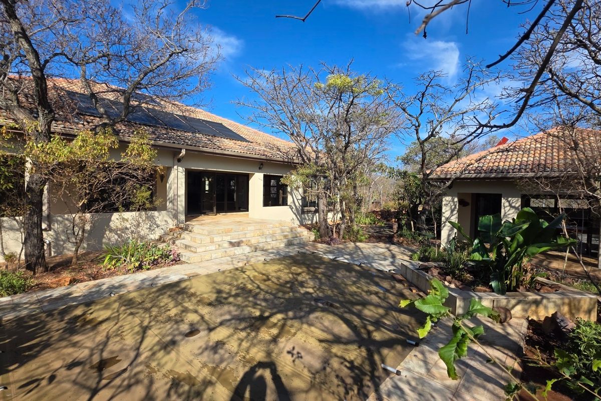 Rear exterior view featuring a stone patio, swimming pool with cover, and a well-maintained garden area with solar panels installed on the tiled roof.