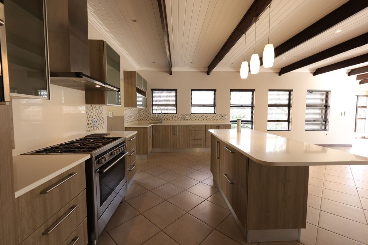 Modern, spacious kitchen featuring a large central island, stone countertops, gas stove, and exposed timber ceiling beams with ample natural light.