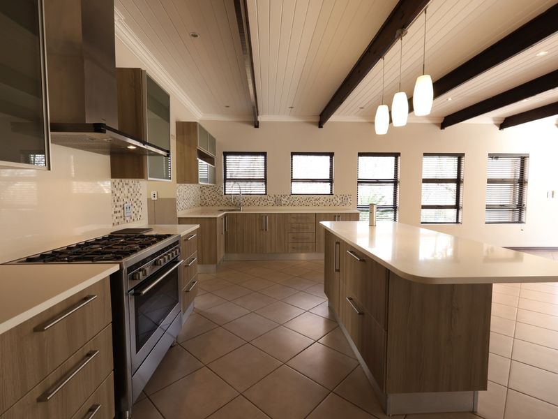 Modern, spacious kitchen featuring a large central island, stone countertops, gas stove, and exposed timber ceiling beams with ample natural light.