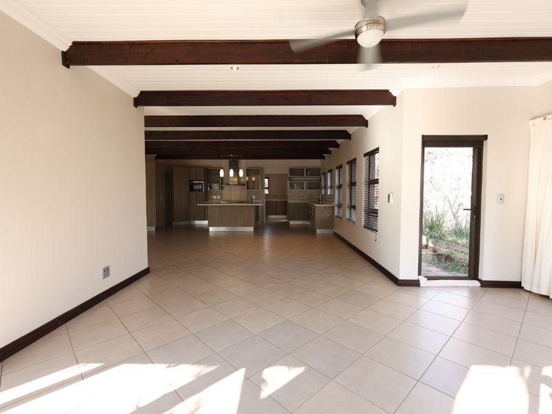 Spacious open-plan living and kitchen area featuring exposed timber beams, tiled flooring, and direct access to the garden through a glass door.