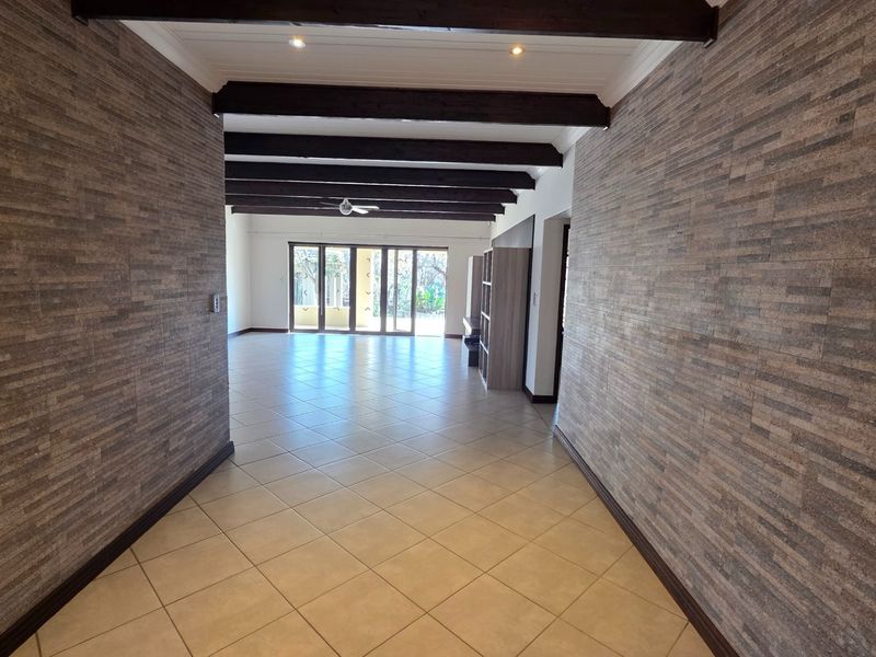 Spacious open-plan living area featuring striking stone-clad walls, exposed timber ceiling beams, and large sliding glass doors leading to the outdoors.