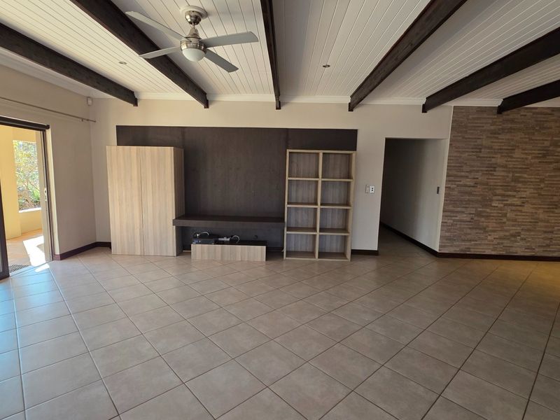Spacious living area featuring exposed timber ceiling beams, tiled flooring, a stone feature wall, and direct access to an outdoor patio through sliding glass doors.