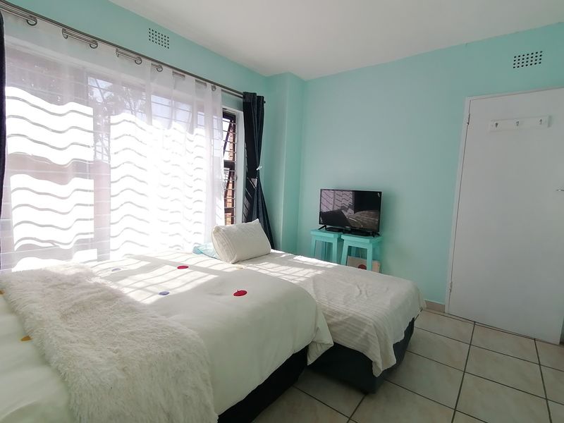 A bright bedroom featuring tiled flooring, a large window allowing natural light, and a standard internal door.