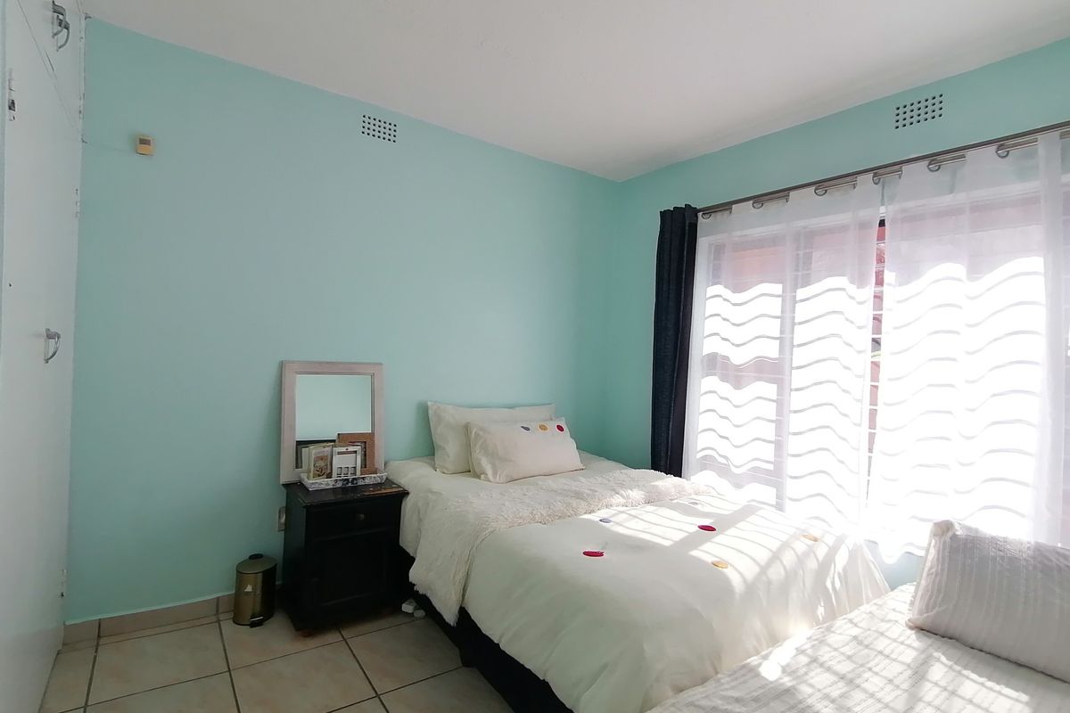 A bedroom featuring light blue walls, tiled flooring, and a built-in cupboard, with natural light entering through a large window.