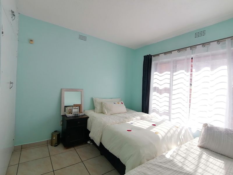 A bedroom featuring light blue walls, tiled flooring, and a built-in cupboard, with natural light entering through a large window.