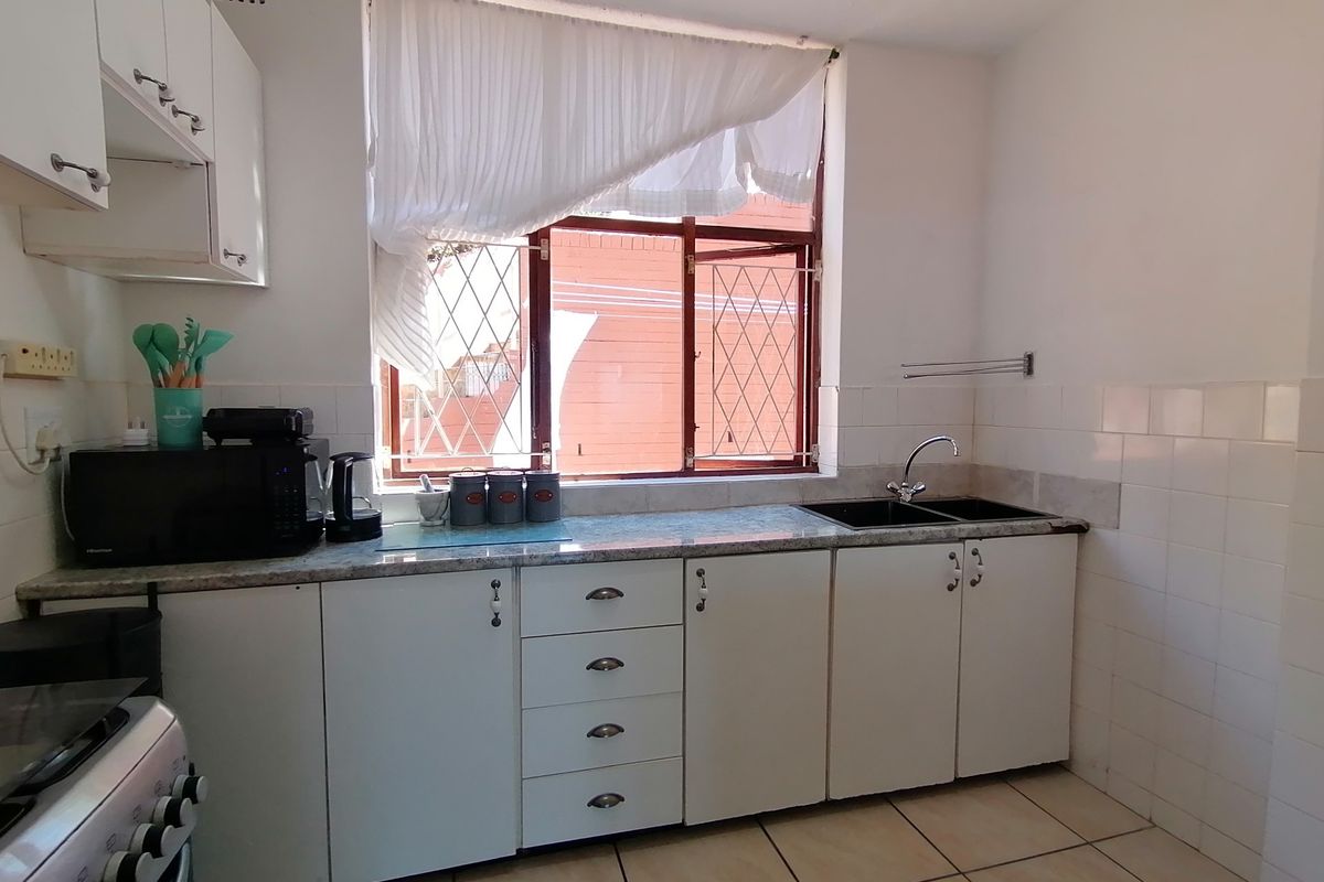 A functional kitchen featuring white cabinetry, laminate countertops, a double basin sink, and tiled flooring with a window providing natural light.