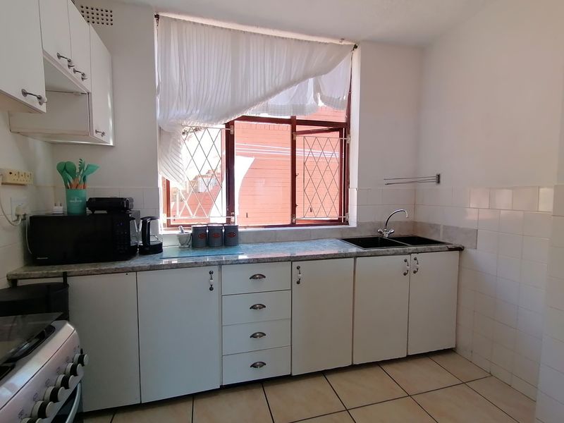 A functional kitchen featuring white cabinetry, laminate countertops, a double basin sink, and tiled flooring with a window providing natural light.