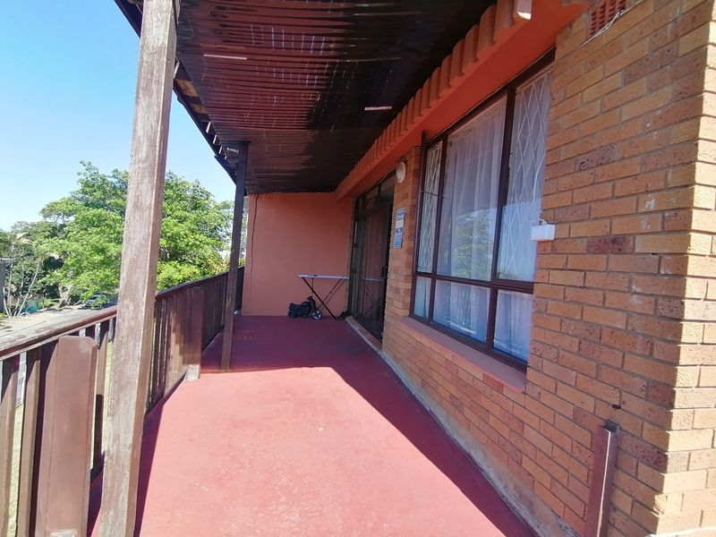 A covered balcony featuring a brick facade, timber balustrade, and sliding glass door access, offering an outdoor space with potential for enhancement.