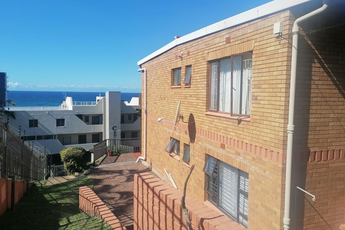 Exterior view of the apartment building featuring face brick construction, paved courtyard area, and ocean views in the background.