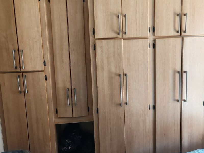A bedroom featuring extensive light wood-finish built-in cupboards providing ample storage space.