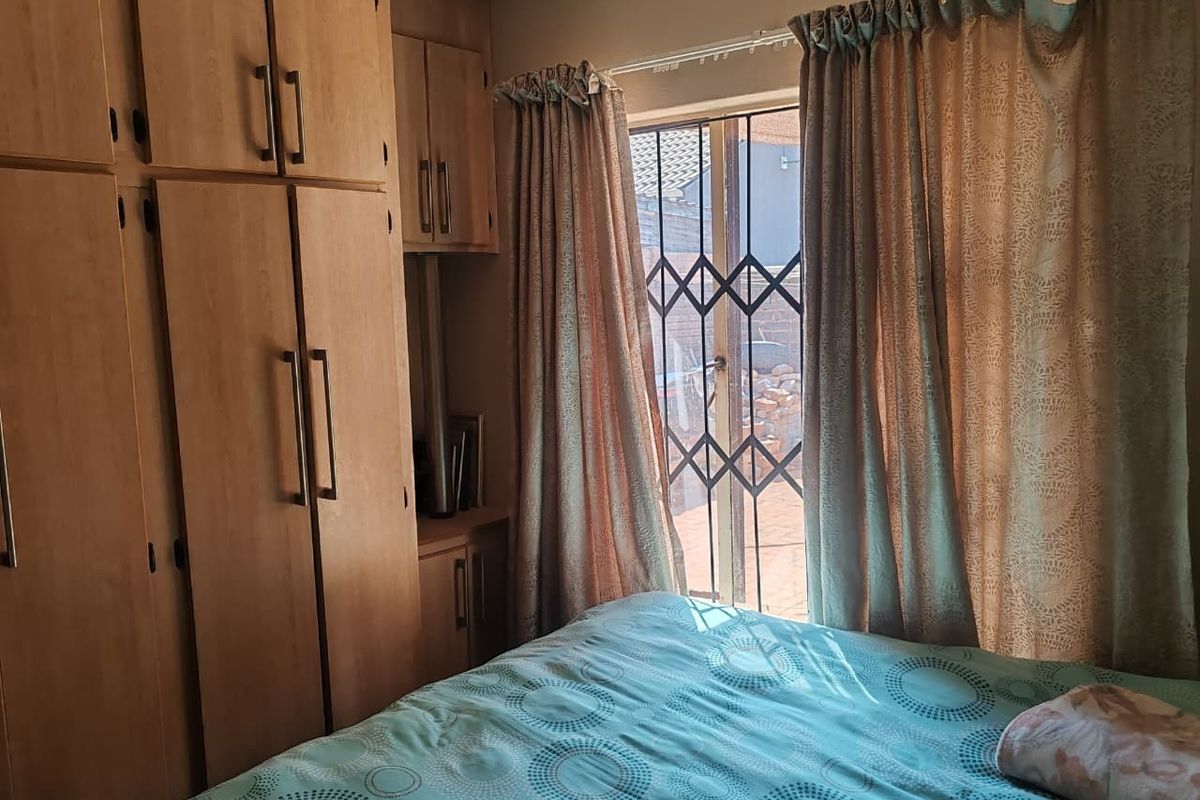 A bedroom featuring built-in wooden cupboards and a sliding door with a security gate, providing access to the exterior.